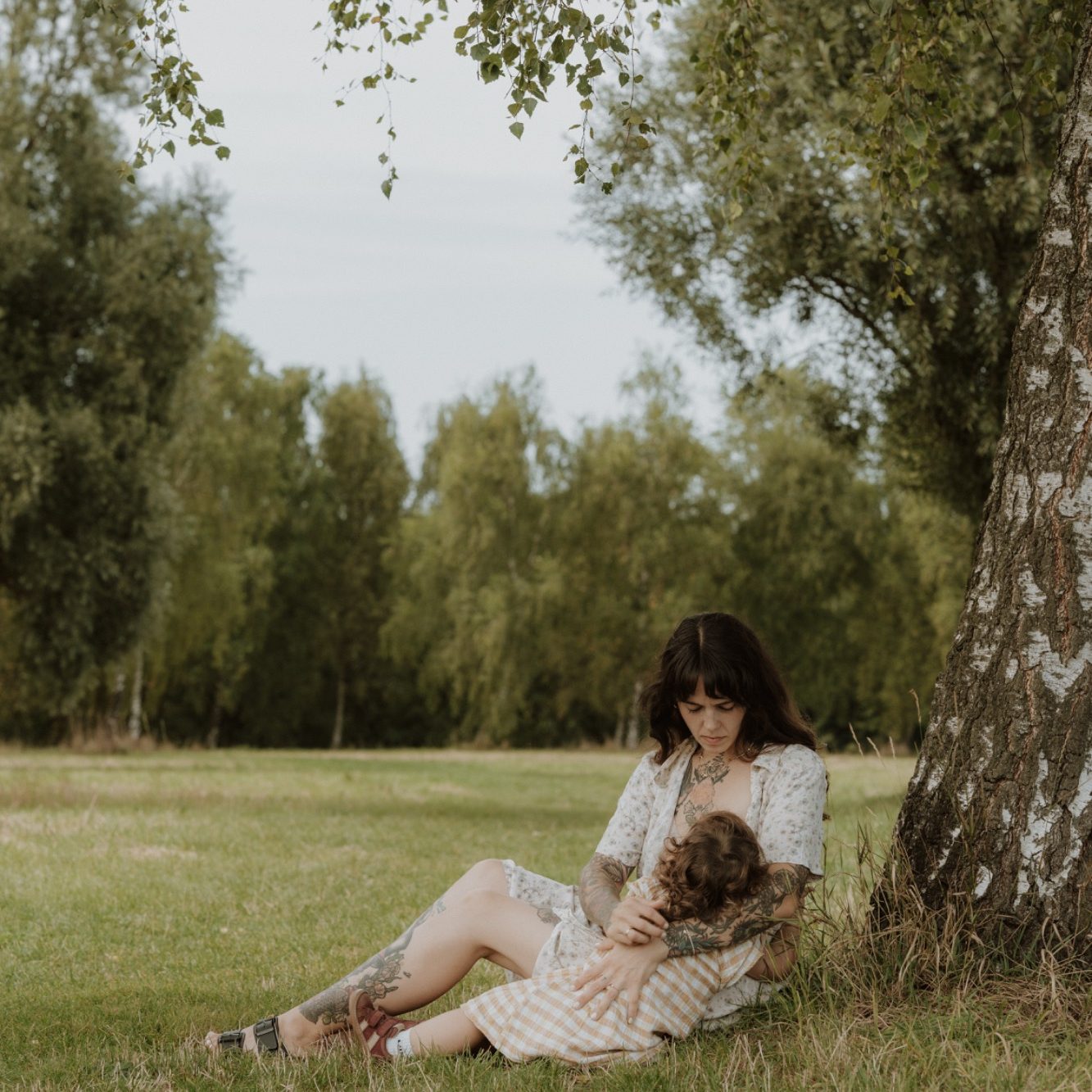 Die Fotografin sitzt als Modell unter einem Baum und hält ein Kind im Gras.