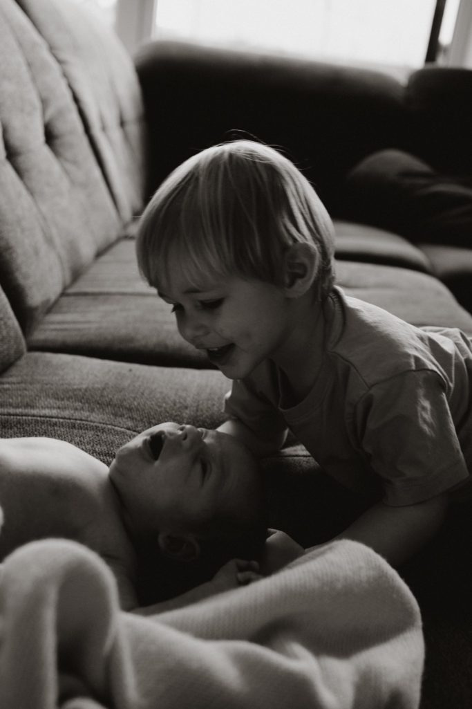 Zwei kleine Kinder liegen auf einem Sofa und lachen miteinander.