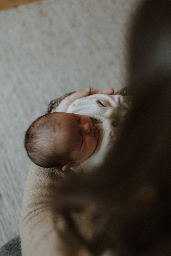 Eine Person hält ein schlafendes Baby in den Armen, von oben betrachtet.