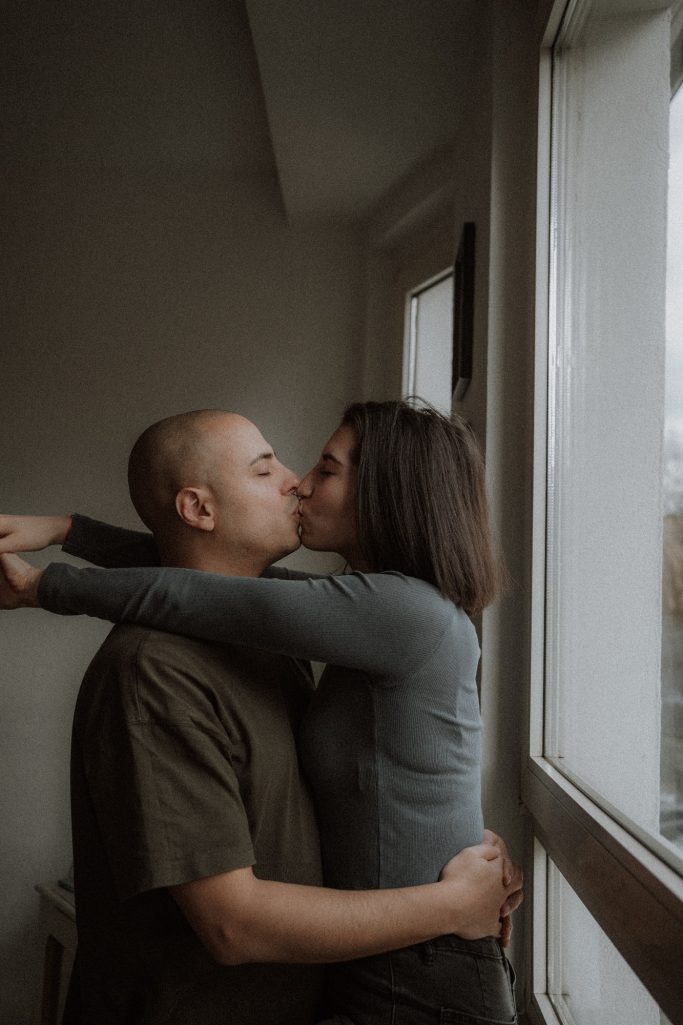 Paar küsst sich liebevoll vor einem Fenster, umarmt und in inniger Zweisamkeit.
