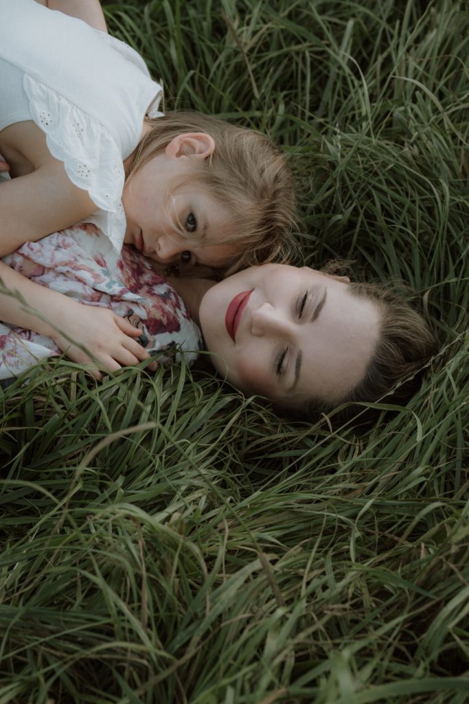 Eine Frau und ein Kind liegen im hohen Gras und lächeln entspannt.