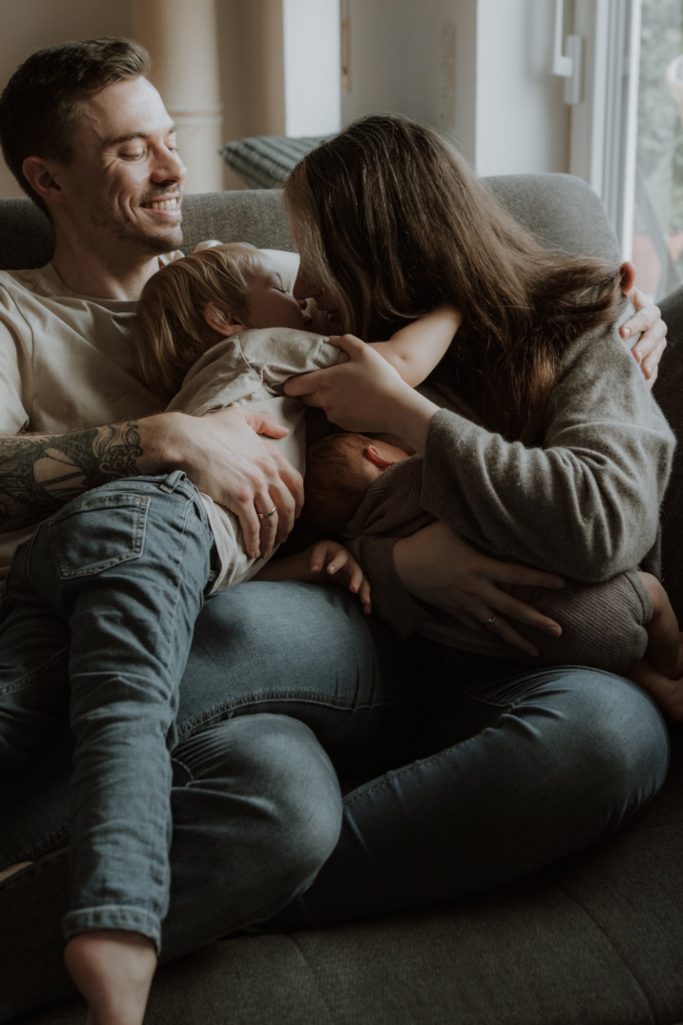 Eine Familie sitzt gemütlich zusammen auf einer Couch und umarmt sich.